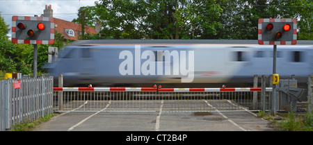 I binari ferroviari rosso lampeggiante spia livello di segno attraversando i cancelli di barriera stradale del paese treni passeggeri motion blur a Margaretting Essex England Regno Unito Foto Stock