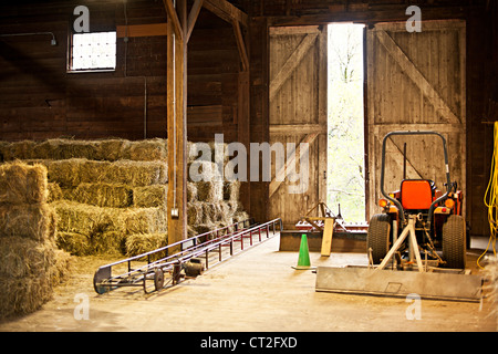 Interno del granaio di legno con balle di fieno di pile e attrezzature agricole Foto Stock