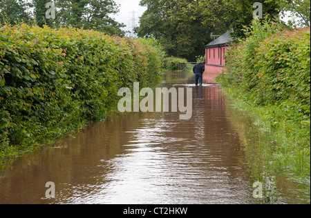 Uomo che cammina attraverso il paese allagato in corsia Vale of Glamorgan Galles del Sud Foto Stock