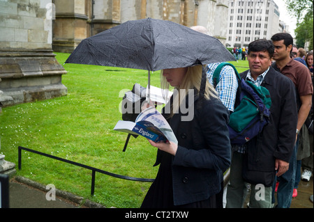 Un turista la lettura di un libro guida in Inghilterra mentre in coda al di fuori dell Abbazia di Westminster London REGNO UNITO Foto Stock