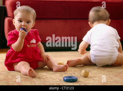 Due bambini seduti sul pavimento a giocare insieme mentre si mette un giocattolo in bocca. Foto Stock