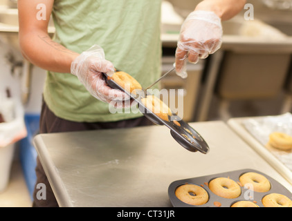Un uomo estrae delicatamente le ciambelle torta da teglie durante la cottura le ciambelle a Tandmen ciambelle, una piccola boutique panificio Missino Foto Stock