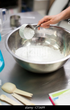 Una donna che mescola insieme gli ingredienti in un grande recipiente durante la cottura le ciambelle a Tandmen ciambelle, un piccolo panificio boutique Foto Stock