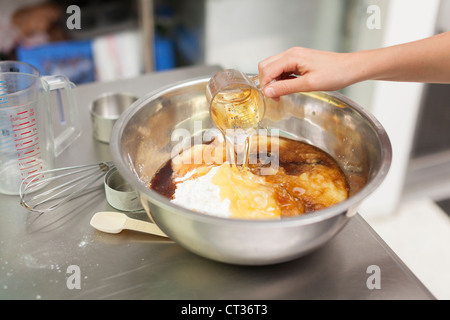 Una donna versa olio come Lei mescola insieme gli ingredienti in un grande recipiente durante la cottura le ciambelle a Tandmen ciambelle, una piccola Foto Stock