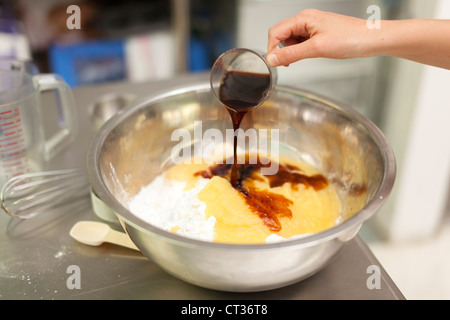 Una donna si riversa di estratto di vaniglia come Lei mescola insieme gli ingredienti in un grande recipiente durante la cottura le ciambelle a Tandmen Doughnu Foto Stock