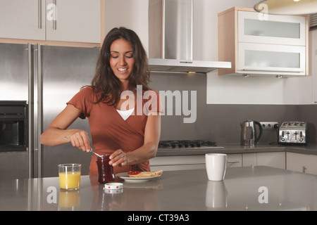 Donna marmellata di spargimento su toast in cucina Foto Stock