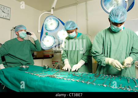 Teatro chirurgico personale posa vari strumenti chirurgici sul piano operativo mentre il chirurgo colloqui sul suo telefono cellulare. Foto Stock