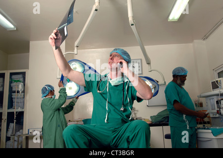 Un chirurgo occupato esamina un x-ray mentre si parla sul suo telefono cellulare Foto Stock