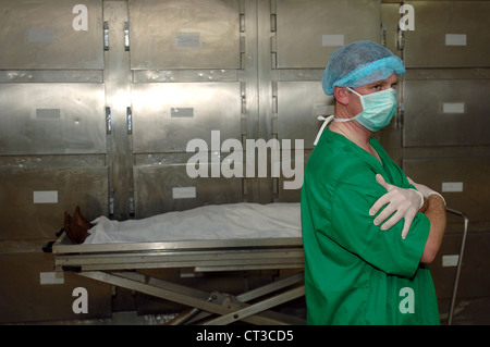 Un tecnico mortuario sorge accanto ad un cadavere su un lettino. Foto Stock