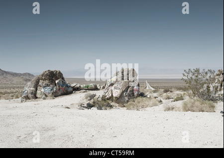 Coperto di graffiti rocce nel deserto di Mojave, California, Stati Uniti d'America. Lungo rettilineo di strada che corre verso l'orizzonte. Foto Stock