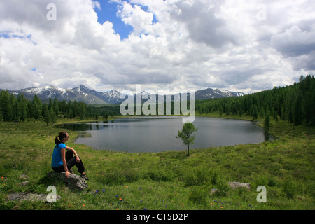 Donna seduta su una roccia da incontaminato lago di montagna, Ulagansky pass, Altai, Siberia, Russia Foto Stock