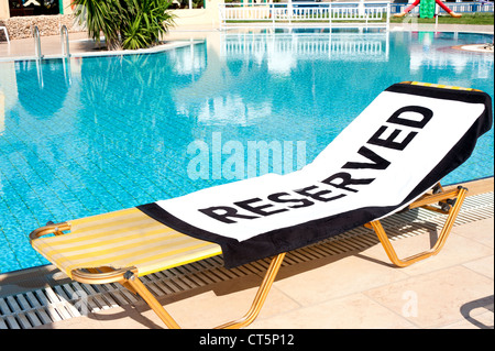 Un telo da spiaggia con la parola 'Riservato' spalmato su un lettino a fianco di una piscina Foto Stock