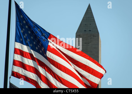 WASHINGTON DC - una bandiera americana vola in primo piano, retroilluminata contro il cielo, con la caratteristica forma a obelisco del monumento a Washington visibile sullo sfondo. Il monumento alto 555 metri, completato nel 1884, onora il primo presidente della nazione, George Washington. La bandiera e il monumento sono due dei simboli nazionali più riconoscibili d'America, entrambi situati sul National Mall nel cuore della capitale della nazione. Il Washington Monument rimane uno dei monumenti più visitati degli Stati Uniti, attirando milioni di visitatori ogni anno. Foto Stock