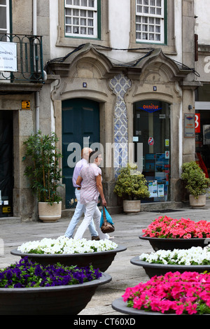 Coppia che cammina davanti a un negozio ornato e ciotole di fiori di nasturtium, Viana do Castelo, Portogallo settentrionale Foto Stock