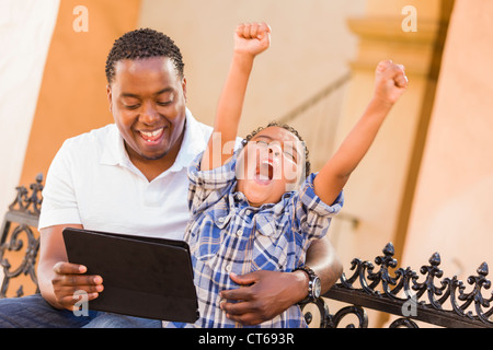 Felice americano africano padre e di razza mista figlio divertirsi usando il Touch Pad computer Tablet all'esterno. Foto Stock