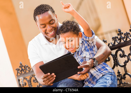 Felice americano africano padre e di razza mista figlio divertirsi usando il Touch Pad computer Tablet all'esterno. Foto Stock