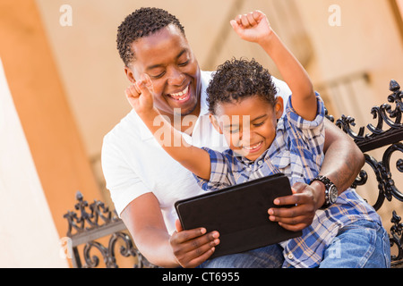 Felice americano africano padre e di razza mista figlio divertirsi usando il Touch Pad computer Tablet all'esterno. Foto Stock