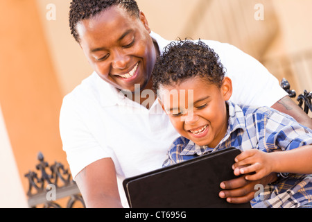 Felice americano africano padre e di razza mista figlio divertirsi usando il Touch Pad computer Tablet all'esterno. Foto Stock