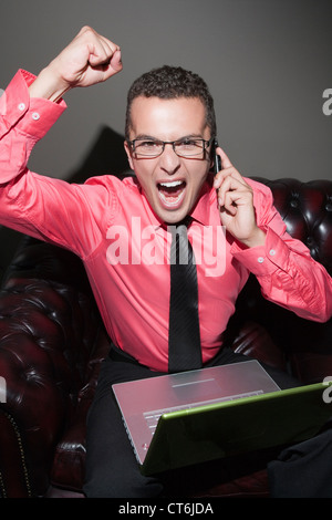 Ritratto di un uomo d affari con computer portatile e il telefono cellulare, che celebra il successo con il pugno chiuso Foto Stock