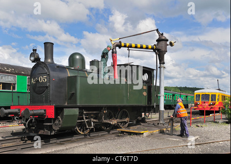 Driver del motore ed equipaggio caldaia di riempimento del treno a vapore dall'acqua gru presso il deposito di Trois Vallées a Mariembourg, in Belgio Foto Stock