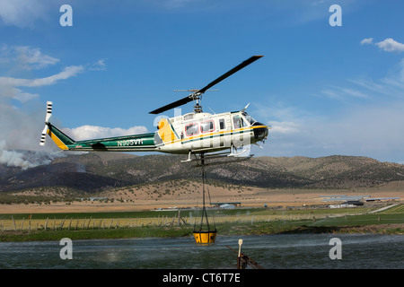 Un vigile del fuoco elicottero precipita per aiutare a mettere fuori un wildfire, portando un grosso secchio di acqua. Foto Stock