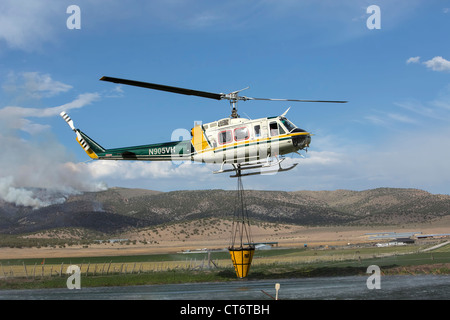 Un vigile del fuoco elicottero precipita per aiutare a mettere fuori un wildfire, portando un grosso secchio di acqua. Foto Stock