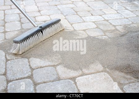 La ginestra di spazzamento di sabbia di bloccaggio nel patio del cortile lastricatori Foto Stock