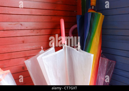 Ombrelloni colorati in piedi contro un rosso e blu di legno verniciato parete. Foto Stock