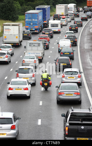 Un motociclo filtri attraverso il traffico pesante sulla autostrada M6 vicino a Stafford code nuovamente la visibilità degli inceppamenti BIKERS DI TRASPORTO ETC REGNO UNITO Foto Stock