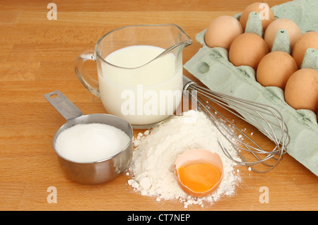 Ingredienti per fare frittelle, zucchero di latte uova e farina con una frusta su un piano di lavoro in legno Foto Stock