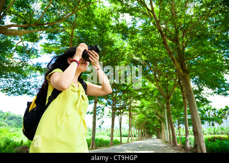 Giovane donna con zaino in piedi nella foresta verde prendendo foto Foto Stock