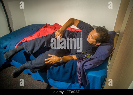 Un giovane uniformata Asiatico-americano pompiere salta precipitosamente dal letto come egli risponde a un allarme a un firehouse in Laguna Niguel, CA Foto Stock