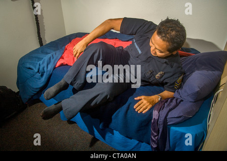 Un giovane uniformata Asiatico-americano pompiere salta precipitosamente dal letto come egli risponde a un allarme a un firehouse in Laguna Niguel, CA Foto Stock