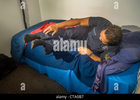 Un giovane uniformata Asiatico-americano pompiere salta precipitosamente dal letto come egli risponde a un allarme a un firehouse in Laguna Niguel, CA Foto Stock