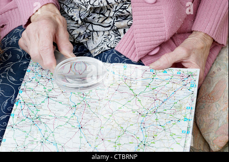 Donna anziana guardando un tradizionale mappa su carta (mappe) di Inghilterra attraverso una lente di ingrandimento Foto Stock