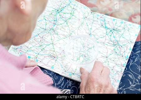 Donna anziana guardando un tradizionale mappa su carta (mappe) di Inghilterra attraverso una lente di ingrandimento Foto Stock