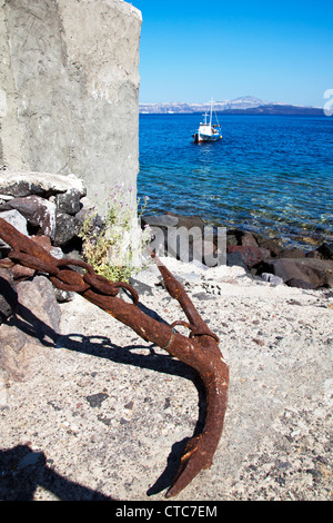 Vecchio arrugginito sinistra di ancoraggio a terra con piccola barca in mare sulla Caldera, Thira, Santorini, isola greca, grecia, Foto Stock