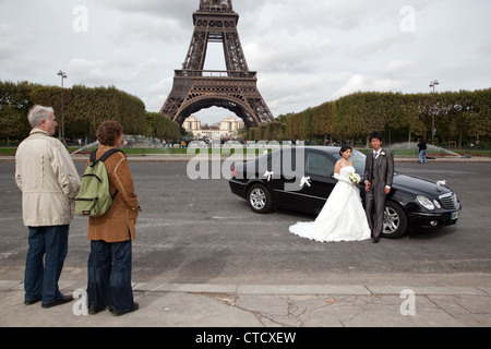 I turisti stranieri guardare una coppia cinese in posa per foto di matrimonio nel Campo di Marte vicino alla Torre Eiffel a Parigi, Francia. Foto Stock