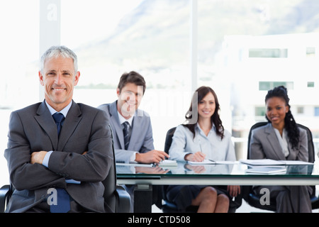 Imprenditore maturo seduto con le braccia incrociate mentre il suo compagno di squadra è dietro di lui Foto Stock