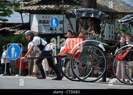 Turisti che cavalcano in risciò a Nara, Giappone. I pulller in risciò indossano stivali da lavoro jika-tabi a due punte Foto Stock