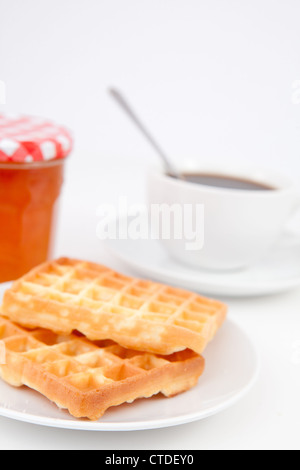 Cialde e tazza di caffè con un cucchiaio su piastre e un vasetto di marmellata Foto Stock