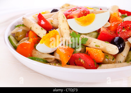 Una ciotola di insalata di pasta con uova, pomodori, cetrioli, arancio pepe e le olive in un condimento di erbe. Foto Stock