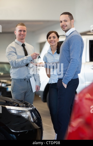 Sorridente venditore di consegnare le chiavi di una coppia felice Foto Stock