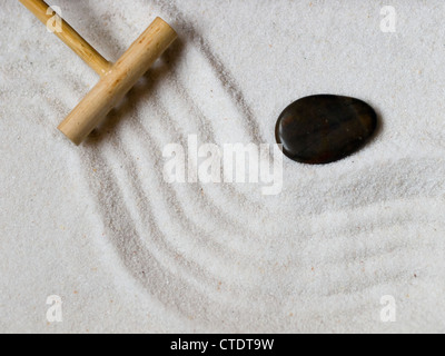 Close-up di un giapponese giardino zen con un rastrello in legno e una pietra nera. Foto Stock