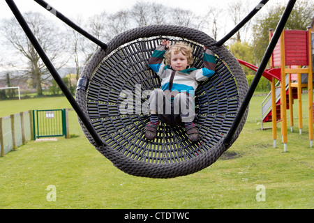 Quattro anni ragazzo biondo su un parco giochi basket swing Foto Stock