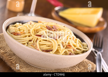 Spaghetti alla carbonara fatta con pancetta, uova, formaggio e pepe nero servito in tazza con formaggio alla griglia nel retro Foto Stock
