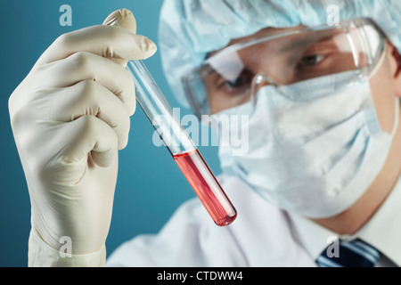 Giovane uomo studiando il campione di liquido contenuto in una provetta Foto Stock