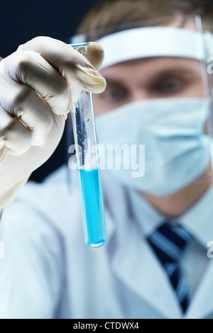 Uomo in uniforme di protezione e guanti in possesso di una provetta con un potenzialmente liquidi pericolosi Foto Stock