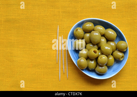 Olive verdi snocciolate sulla piastra blu sulla tovaglia giallo Foto Stock