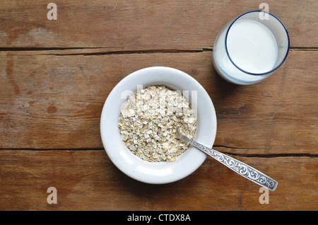 Oat-fiocchi in bianco ciotola e latte in vetro blu sull'annata tavolo in legno Foto Stock